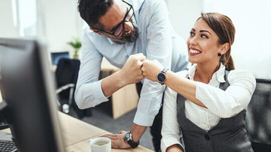 Migrazione in Cloud: colleghi felici fanno gesto di collaborazione sorridendo alla scrivania