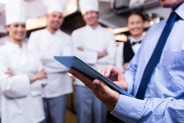 F&B Manager parla allo staff in cucina con un tablet in mano.