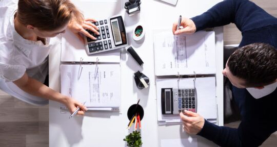 Aggiornamenti Fatturazione Elettronica, due colleghi calcolano fatture con calcolatrici alla scrivania