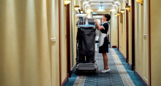 cover blog Software para la limpieza de habitaciones - Camarera de hotel en el pasillo con carrito y utensilios de limpieza