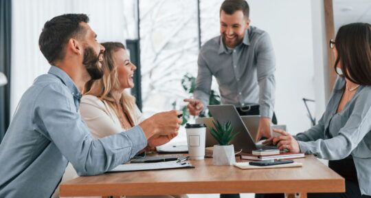 PDM in ERP persone che discutono sorridendo in ambito lavorativo sedute a un tavolo d'ufficio